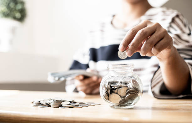 une femme met des pièces dans un bocal avec beaucoup de pièces à l’intérieur, elle parse de diviser son argent pour économiser de l’argent et l’investir pour le faire croître encore plus. concept d’économie d’argent et d’investissement. - gold paying internet credit card photos et images de collection