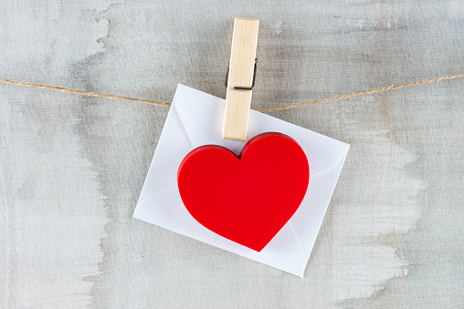 Red colored heart shape attached to white envelope hanging on a clothesline