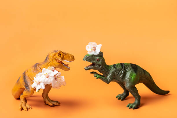 dinosaur de jouet tyrannosaurus retenant la fleur d’abricot dans ses pattes sur le fond orange - dinosaur toy dino monster photos et images de collection