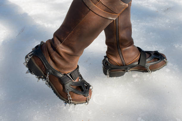 Steel traction cleats for ice on female leather booths on icy hiking trail in Canada In early spring, roads and trails in rural areas of Canada are often covered by thick ice. Steel traction cleats help to prevent injuries caused by falling. studded footwear stock pictures, royalty-free photos & images