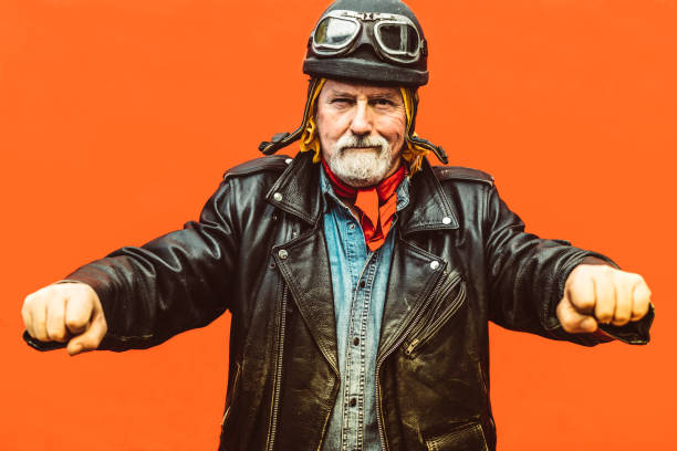 Old biker wearing leather jacket, hat and sunglasses simulating to drive his motorcycle. - Concept of enjoying life at every age