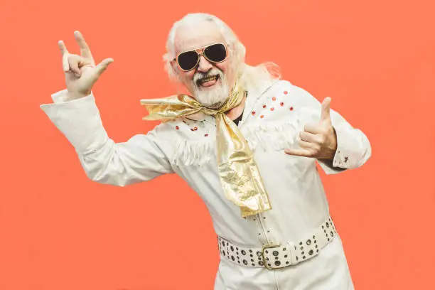 Photo of Old dressed up man pensioner who loves rock'n'roll, dancing and having fun on a living coral background - Concept of enjoying life at every age
