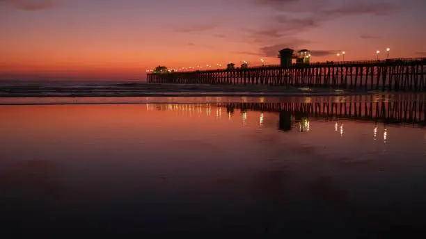 Photo of Pier silhouette Oceanside California USA. Ocean tide tropical beach. Summertime gloaming atmosphere.