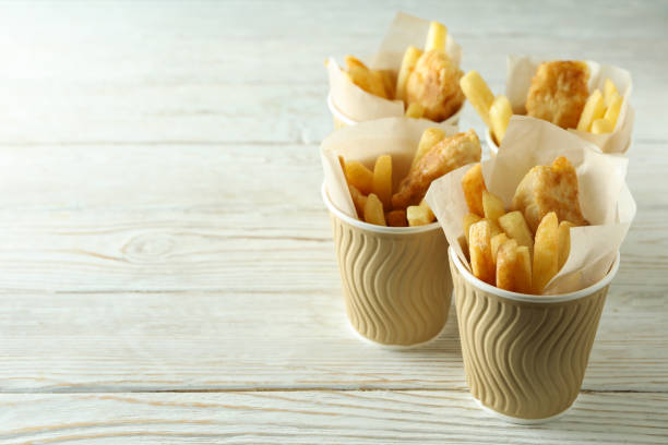 Paper cups with fried fish and chips on wooden background