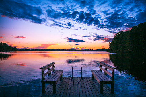 Perspective view of a wooden pier with chairs on the lake at sunset in Finland