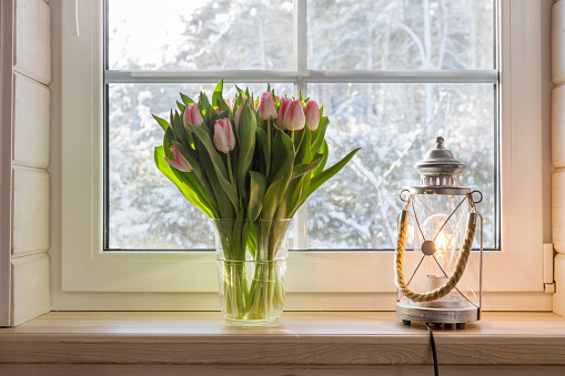 Bouquet of beautiful pink tulips on a wooden windowsill. White window in a Scandinavian style wooden house overlooking the garden, pine forest. Spring concept, Happy 8 March, Women's Day
