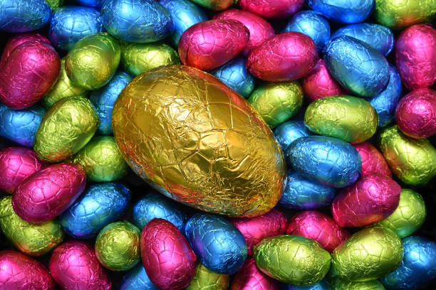 istock Pile or group of multi colored and different sizes of colourful foil wrapped chocolate easter eggs in pink, blue, yellow and lime green with a large gold egg in the middle. 1306996472