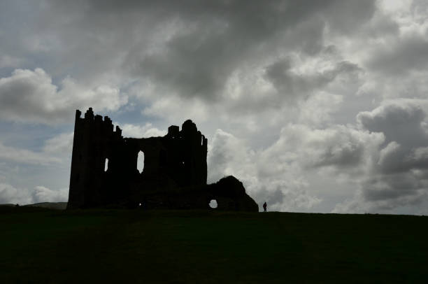 istock Ancient irish castle under a cloudy sky and a tourist. 1307005047