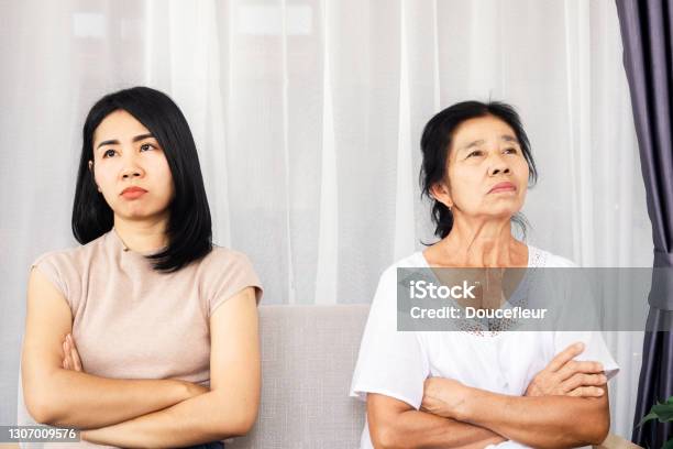 Depressed Asian Mother And Daughter Sitting At Sofa Angry Quarrel Ignoring Each Other Serious Relationship In Family Stock Photo - Download Image Now