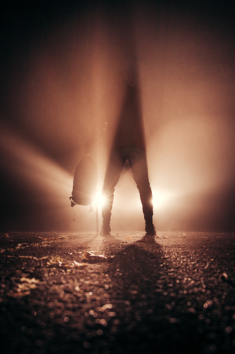 In the glare of car headlights, a man stands motionless, rushing with confidence and a backpack in one hand. Visual effect with different type of light. Sports photo at night