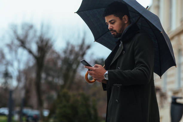 istock Businessman with umbrella texting to client on smartphone 1307013349