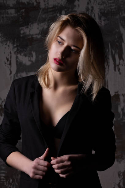 istock Portrait of seductive blonde model wearing black jacket, posing at studio with shadows on her body 1307016253