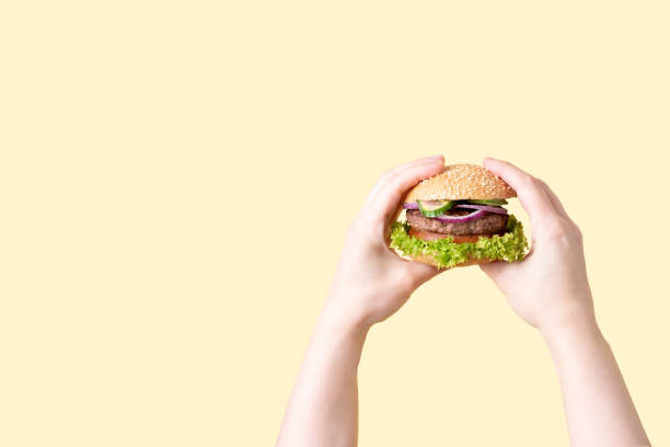 istock Two female hands holding delicious beef burger on the yellow background. 1307018953