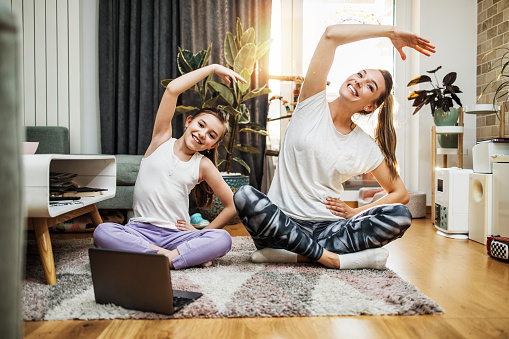 Beautiful young mother practicing fitness exercising and yoga together with her adorable little son. They are enjoying, playing and smiling.