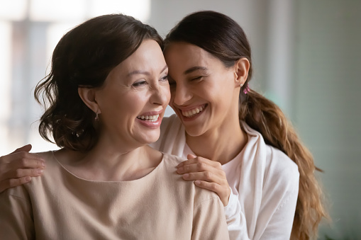 Close up overjoyed middle aged mother and grownup daughter cuddling, enjoying tender moment, leisure time, excited young woman touching mature mum shoulders, good family relationship, two generations