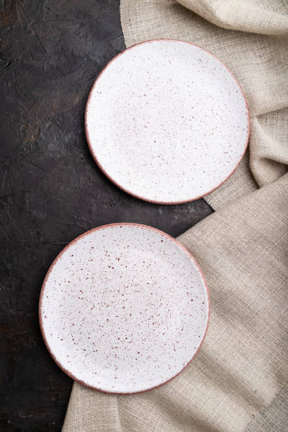 istock Two empty white plates on black concrete background and linen textile. Top view, close up, flat lay. 1307021429