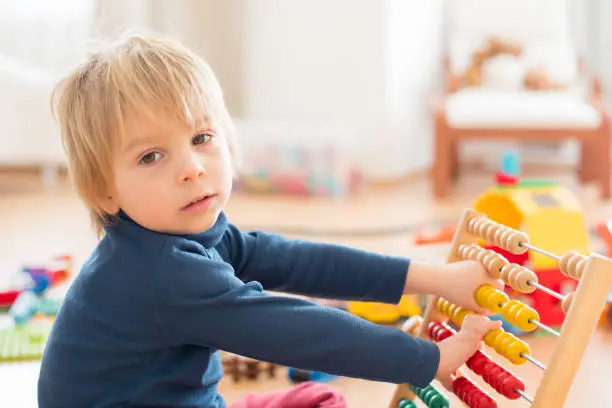 Sweet blond preschool child, toddler boy, playing with abacus at home,construction on the floor behing him