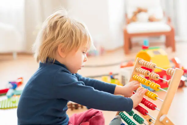 Sweet blond preschool child, toddler boy, playing with abacus at home,construction on the floor behing him