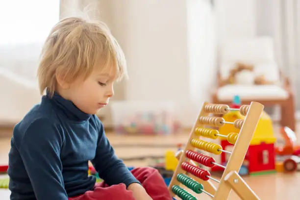 Sweet blond preschool child, toddler boy, playing with abacus at home,construction on the floor behing him