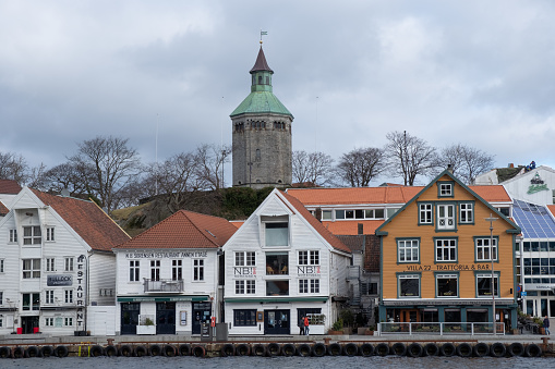 Stavanger, Norway: a winter city centre view of the harbour front area of fjord waterside with shops, bars, hotels and traditional wooden housing architecure. A watchtower historical monument is seen on the skyline