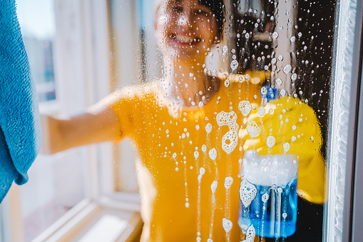 Happy smiling woman washing windows in the apartment