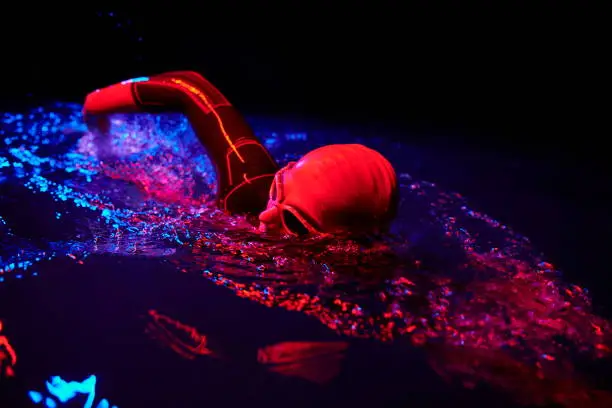 authentic triathlon swimmer have extreme training on dark night wearing wetsuit neon gel color lights