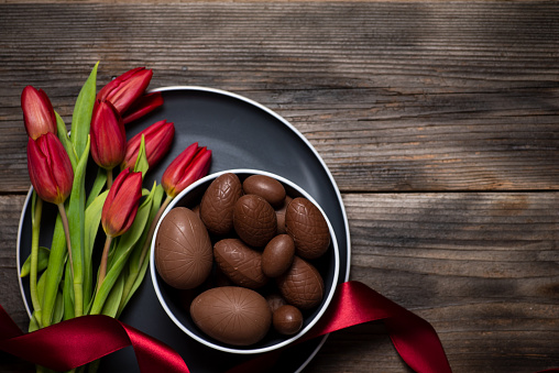 Chocolate Easter eggs in a bowl with red tulip flowers in blossom on a wooden top view
