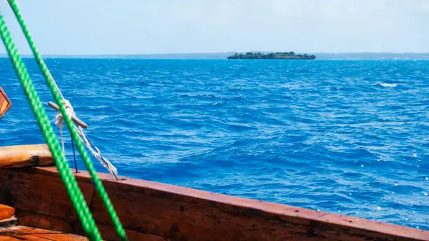 Photo of Part of old traditional african wooden boat in trip on Indian Ocean, Zanzibar, Tanzania, Africa. Beautiful blue splash. Selective focus. Motion blur.