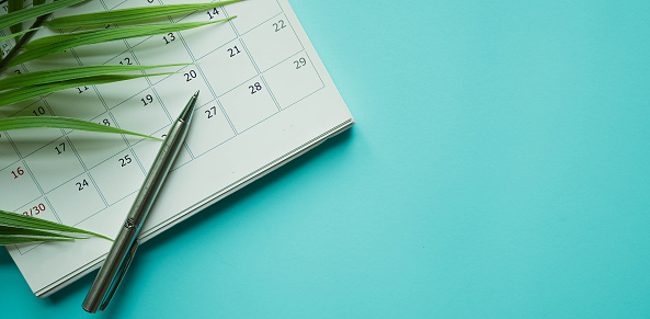 vista de primer plano en el calendario blanco con lápiz y hojas tropicales sobre fondo de mesa azul para planificar el trabajo y el equilibrio de la vida en el concepto de verano de vacaciones photo