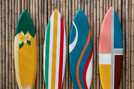 Many different colorful surfboards standing in a row on bamboo wooden wall