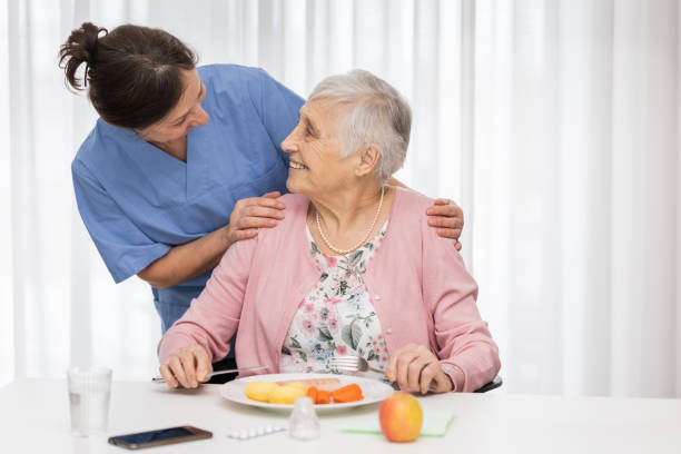 シニア女性と一緒にホーム介護者、食事を提供 - senior adult nursing home eating home interior ストックフォトと画像