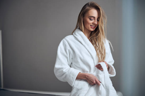 Pleased client getting ready for a beauty procedure Smiling beautiful young woman with loose long hair tying the bathrobe belt at the waist bathrobe photos stock pictures, royalty-free photos & images