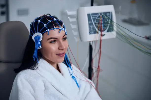 Smiling young woman with a silicone cap on her head dreaming away during the electroencephalography