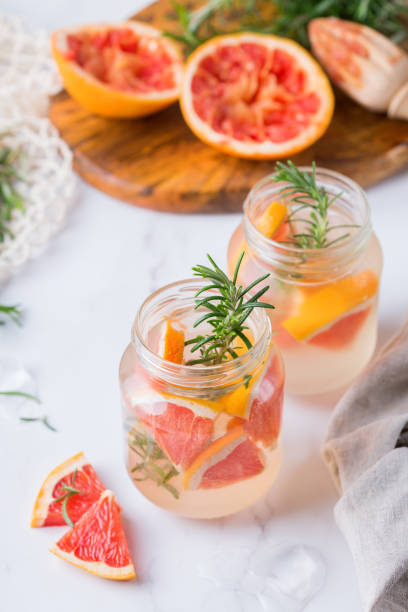 Hard seltzer cocktail with grapefruit and rosemary Hard seltzer cocktail with grapefruit, rosemary and ice on a table. Summer refreshing beverage, drink on a white table soda water glass lemon stock pictures, royalty-free photos & images