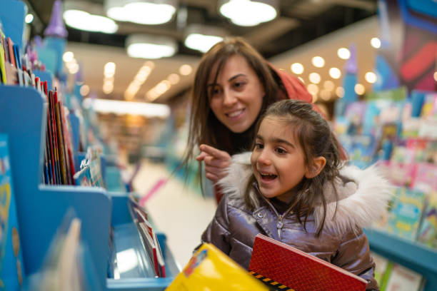 Little girl is delighted when her mother shows where the book her daughter wants in the bookstore Little girl is delighted when her mother shows where the book her daughter wants in the bookstore bookstore book library store stock pictures, royalty-free photos & images