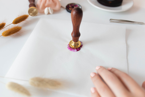 Girl melting some wax to seal an envelope on white table