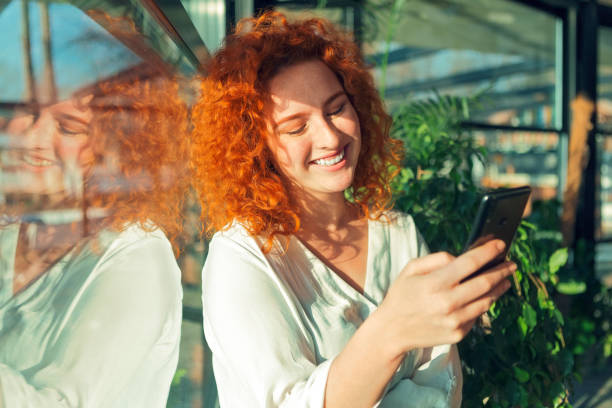 istock Smiling Beautiful redhead young woman using smart phone in cafe 1307058426