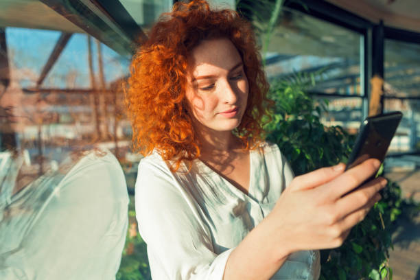 istock Beautiful redhead serious looking young woman using smart phone in cafe 1307058443