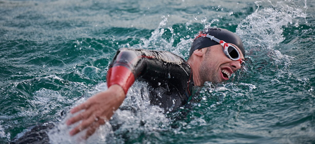 triathlon athlete swimming on beautiful morning sunrise training in lake wearing wetsuit concept of strength and endurance