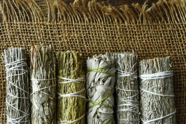 A top view image of several healing sage smudge bundles on burlap fabric.