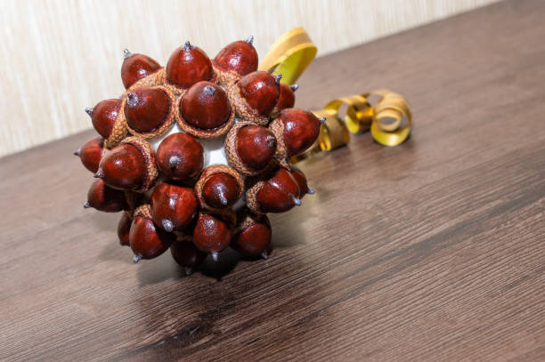 Handmade DIY ball - round brown Christmas decoration from oak acorns on the golden string, yellow background