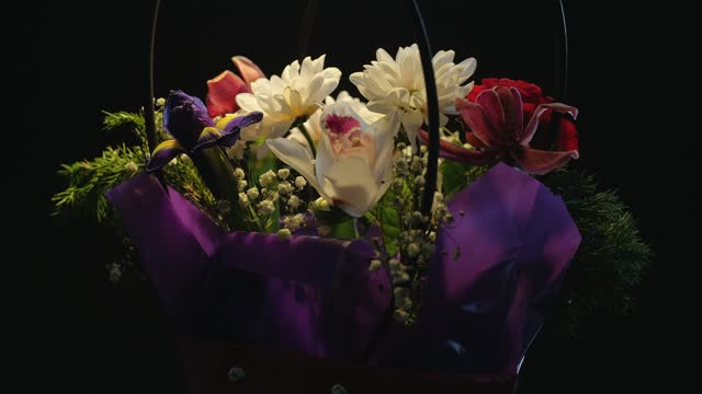 A bouquet of flowers slowly rotates clockwise, on a black background. Gift box with flowers, close-up