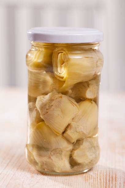 Glass jar with preserved artichoke hearts on wooden table