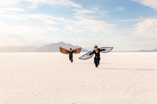 Two young business boys dressed in business suits and wings imagine flying their business into the sky, with profits and growth. Image taken at the Bonneville Salt Flats, Utah, USA.