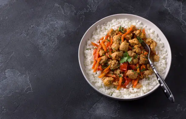 Photo of Vegan stew soy meat and vegetables served with boiled rice and greens on black textured background