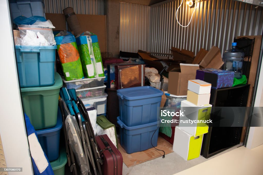A storage unit full of boxes and plastic tubs Interior of a self storage unit in a warehouse filled to the brim with belongings and junk Storage Compartment Stock Photo