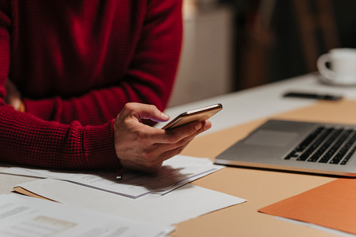 An unrecognizable businessman in a red sweater using his mobile phone at the office late at night.