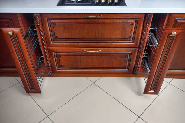 istock Pull out spice rack cabinet filler pantry. Two vertical drawers for spices shelf under countertop with wooden panel and hob. Classic style kitchen with golden elements cherry alder wood cabinetry. 1307095032