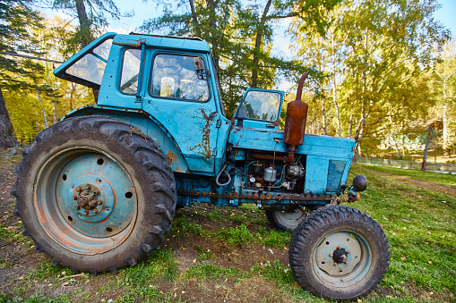 An old blue tractor stands in a farmyard.