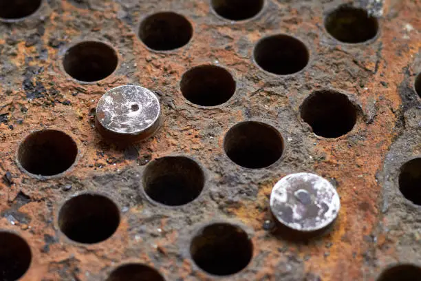 Photo of Tube sheet or plate of heat exchanger boiler closeup selective focus background disconnected muted clogged leaky tubes with steel plugs with insoluble hard mineral deposits salts scale and corrosion.